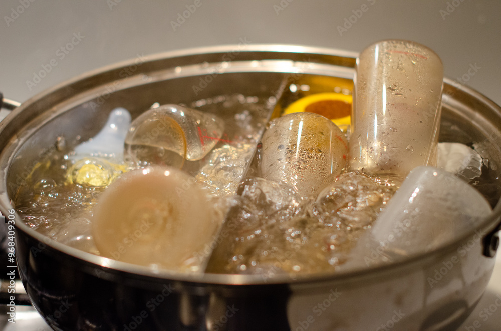 A pot of boiling water with baby bottles and accessories submerged in it. a process of sterilizing baby items. A pot of boiling water with baby bottles and accessories submerged in it. a process of sterilizing baby items.