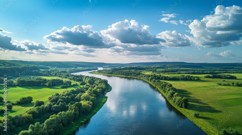 Obraz premium A serene river winding through lush green landscapes under a bright blue sky with clouds.