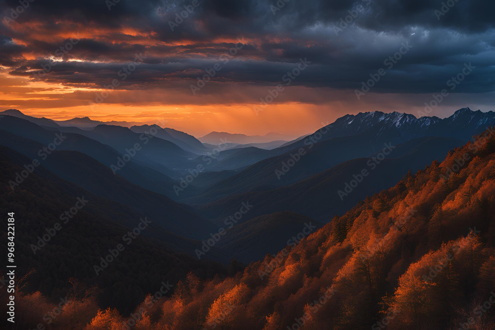 Obraz premium Orange glow of twilight from behind the silhouetted mountain ridge with dramatic blue-grey clouds in the sky