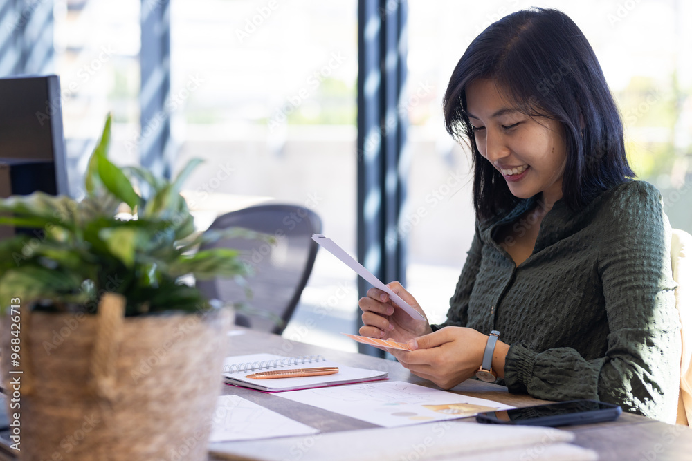 In office, Using tablet and smiling, asian woman working at desk with notepad and plant In office, Using tablet and smiling, asian woman working at desk with notepad and plant