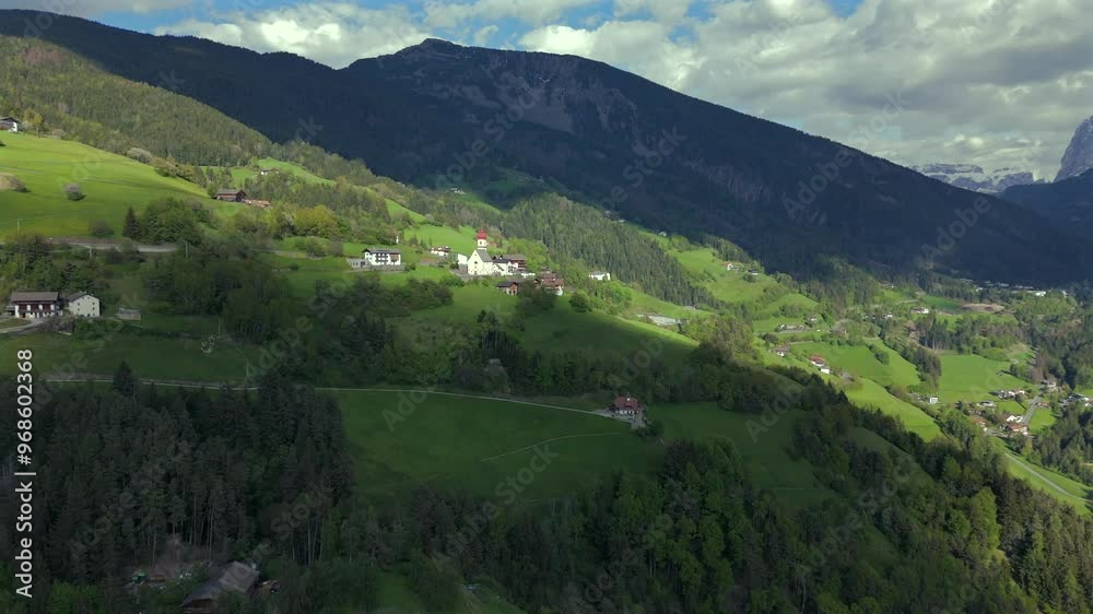 A stunning aerial view of a peaceful village nestled in green hills, surrounded by forest and mountains under a partly cloudy sky. A stunning aerial view of a peaceful village nestled in green hills, surrounded by forest and mountains under a partly cloudy sky.