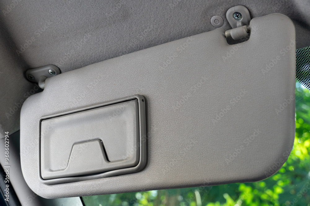 Son visors of car close the glass panel. Front view of the driver inside car. Background of green leaves of trees. Son visors of car close the glass panel. Front view of the driver inside car. Background of green leaves of trees.