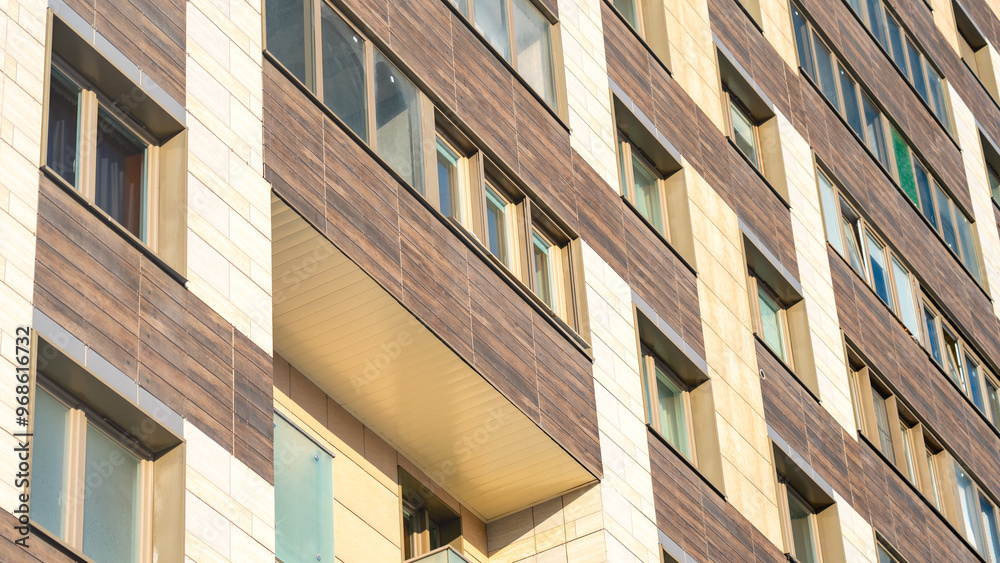 A large brown building with many windows. The windows are mostly clear, but some are tinted. The building appears to be a residential building with a balcony A large brown building with many windows. The windows are mostly clear, but some are tinted. The building appears to be a residential building with a balcony