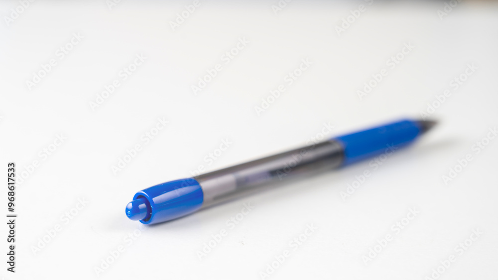 A blue pen with a black tip sits on a white surface. The pen is not in use and is laying on its side. Concept of simplicity and minimalism A blue pen with a black tip sits on a white surface. The pen is not in use and is laying on its side. Concept of simplicity and minimalism