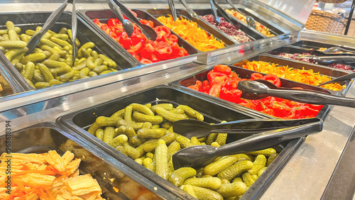 A salad bar with many different types of vegetables, including pickles. The vegetables are arranged in several bowls, and there are several spoons for picking up the food