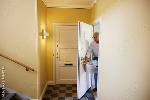 Senior man holding laundry basket and opening room door