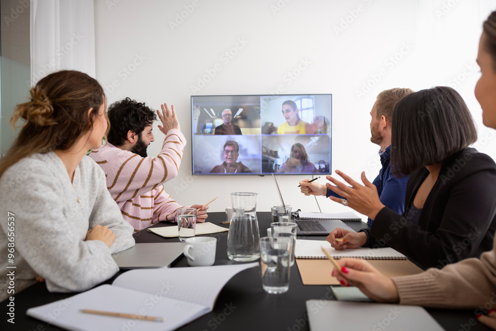 Entrepreneurs greeting team mates on virtual meet while sitting in meeting room at office Entrepreneurs greeting team mates on virtual meet while sitting in meeting room at office