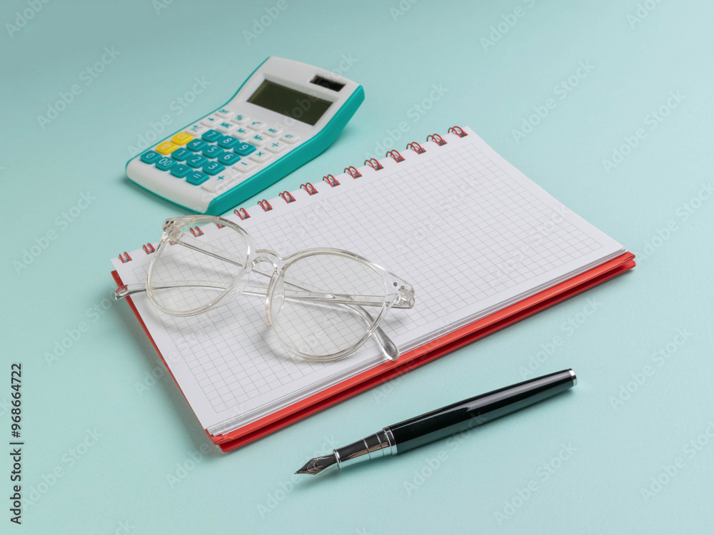 Glasses on Notebook with Pen and Calculator on Turquoise Background - Office Supplies Glasses on Notebook with Pen and Calculator on Turquoise Background - Office Supplies
