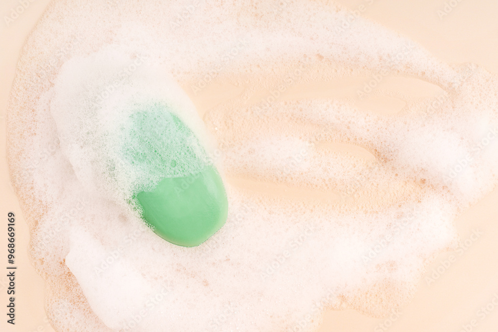 Fototapeta premium Top view of one scented organic antibacterial soap bar of green colour wet, soapy and covered with white foam bubbles on beige background with copy space used as everyday cosmetics for skin hygiene