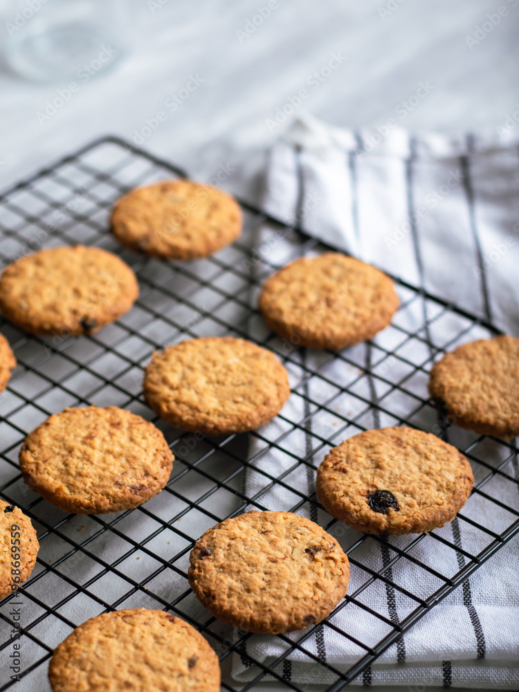 Freshly baked oatmeal cookies cooling on a black wire rack, with a light background and soft natural lighting. The cookies are golden brown with hints of raisins and a crispy texture, creating a cozy Freshly baked oatmeal cookies cooling on a black wire rack, with a light background and soft natural lighting. The cookies are golden brown with hints of raisins and a crispy texture, creating a cozy
