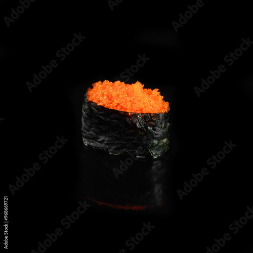 Close-up of delicious tobiko sushi with rice and seaweed wrap on black background, highlighting the vibrant orange fish roe. photo