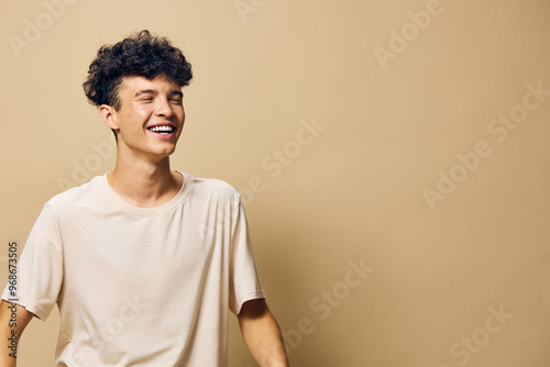 Принти на полотні Smiling young man in a light beige t shirt against a soft brown background, expr