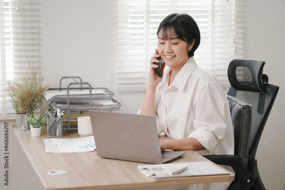 Smiling businesswoman in office, talking on phone with laptop nearby Smiling businesswoman in office, talking on phone with laptop nearby