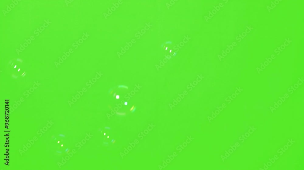 A bright close-up of soap bubbles falling down and sparkling against a green screen backdrop, with fine reflections and fluid motion, perfect for chroma keying and visual effects.