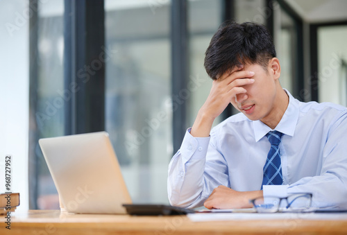 Exhausted young man with laptop in office. Stressed and tired young businessman working with laptop. Asian male feel eyes strain.