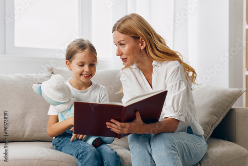 Mother and daughter bonding moment, reading a book together on a cozy living room couch photo