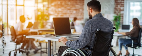 Man in wheelchair working on laptop in modern office. photo