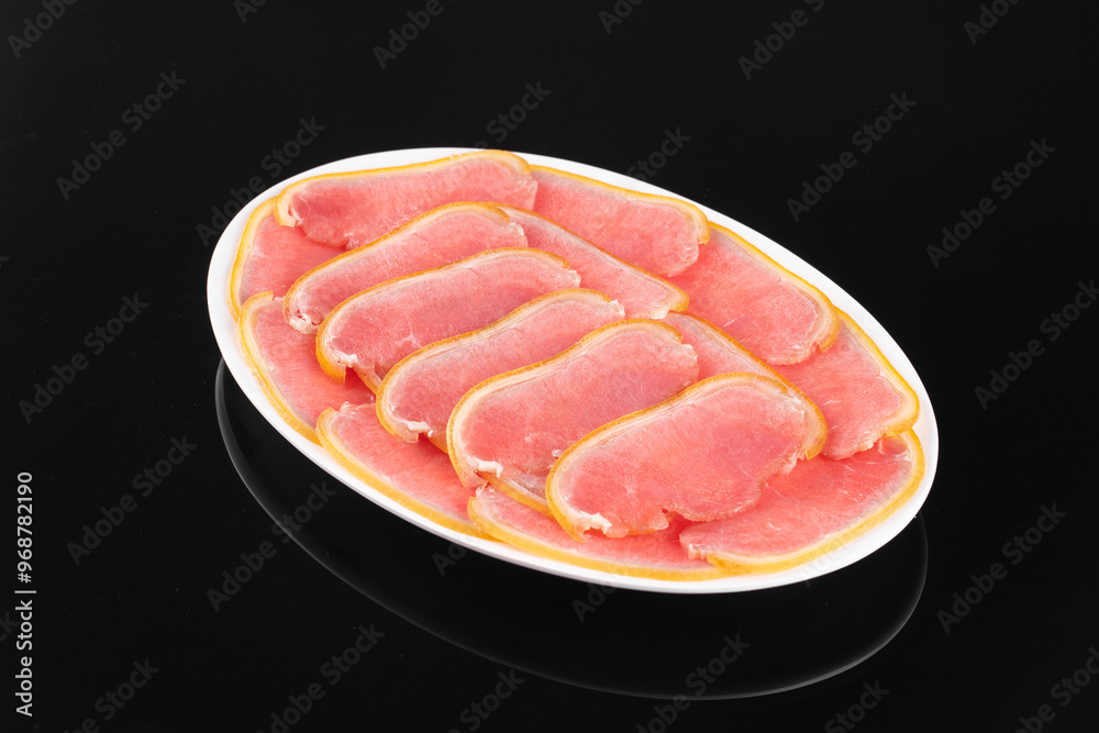 Thinly sliced raw pork displayed on a white plate against a black background. Fresh meat perfect for culinary use.