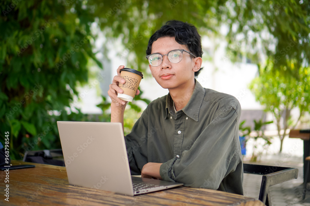 Young asian man thinking while looking to his laptop. Man working on his laptop at the outdoor cafe in the morning Young asian man thinking while looking to his laptop. Man working on his laptop at the outdoor cafe in the morning