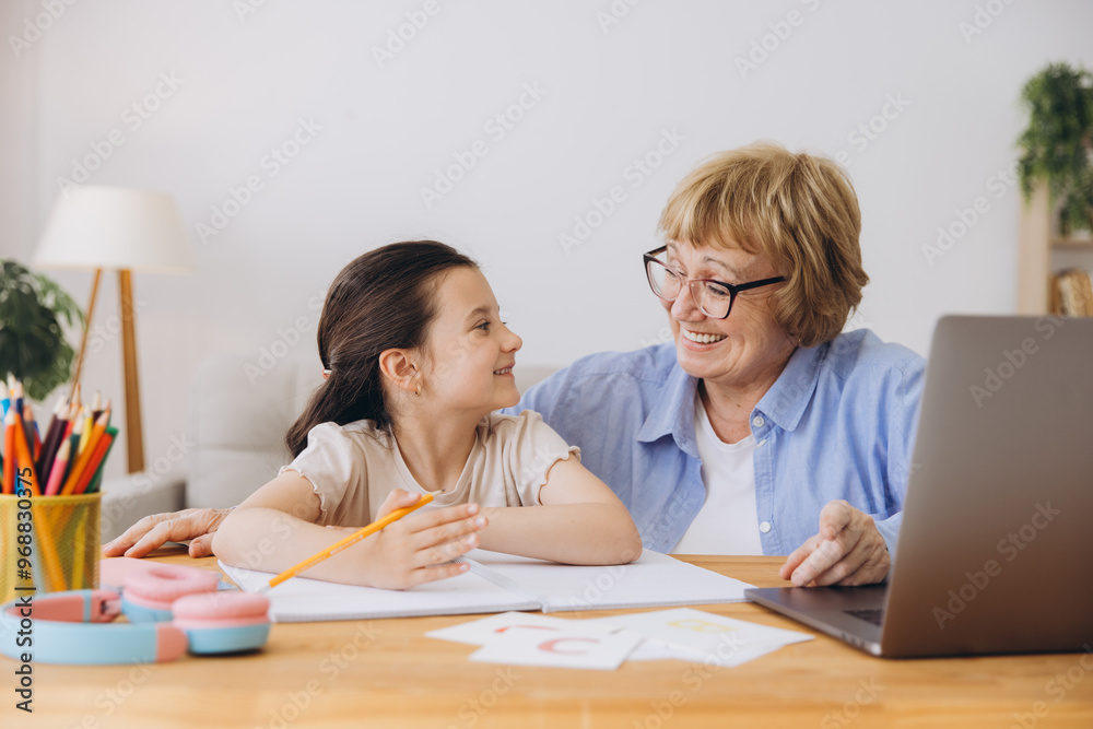 Happy grandma helping adorable preschool granddaughter school kid with homework task. Positive school pupil girl and granny reading learning book at laptop together, enjoying education at home Happy grandma helping adorable preschool granddaughter school kid with homework task. Positive school pupil girl and granny reading learning book at laptop together, enjoying education at home