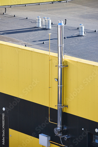 Aluminum composite panels yellow and blue commercial building facade with stainless steel chimney pipe and natural gas duct pipeline of industrial boiler room with stairs under clear blue sky .