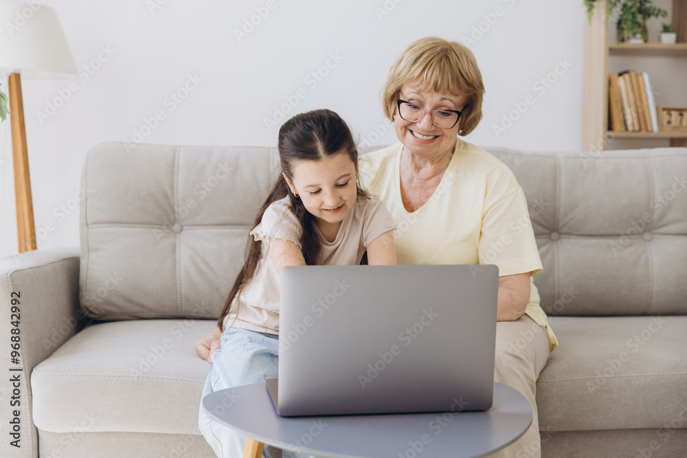 Multi generational family, grandma and granddaughter sit on couch with wireless computer, look at each other with tenderness and love, enjoy leisure on internet and time together, watch on-line movies Multi generational family, grandma and granddaughter sit on couch with wireless computer, look at each other with tenderness and love, enjoy leisure on internet and time together, watch on-line movies