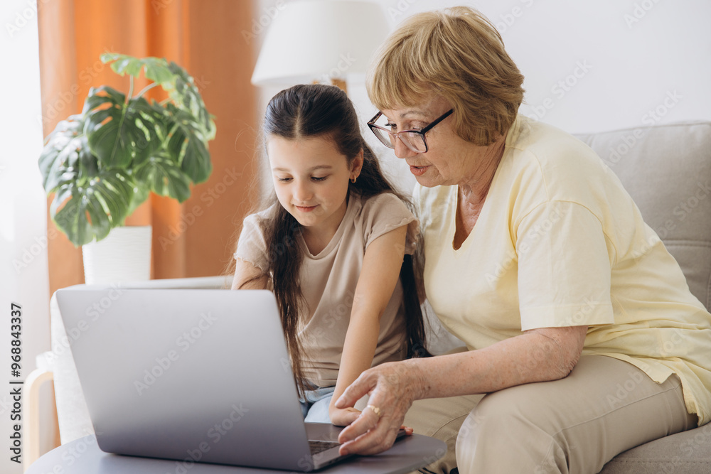 Multi generational family, grandma and granddaughter sit on couch with wireless computer, look at each other with tenderness and love, enjoy leisure on internet and time together, watch on-line movies Multi generational family, grandma and granddaughter sit on couch with wireless computer, look at each other with tenderness and love, enjoy leisure on internet and time together, watch on-line movies