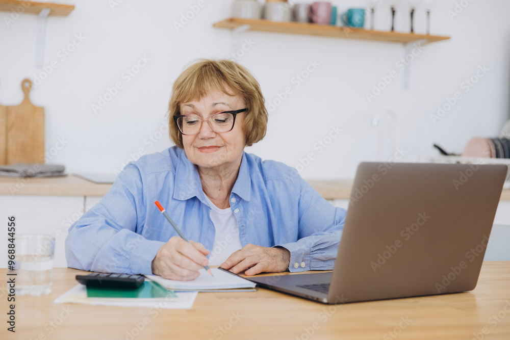 Senior business woman holding paper bill using calculator, old lady managing account finance, calculating money budget tax, planning banking loan debt pension payment sit at home kitchen table. Senior business woman holding paper bill using calculator, old lady managing account finance, calculating money budget tax, planning banking loan debt pension payment sit at home kitchen table.