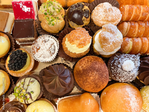 The image shows a tray filled with a variety of pastries. There are different types, including some topped with powdered sugar, fruits like blackberries, and others that appear to be glazed. Some past
