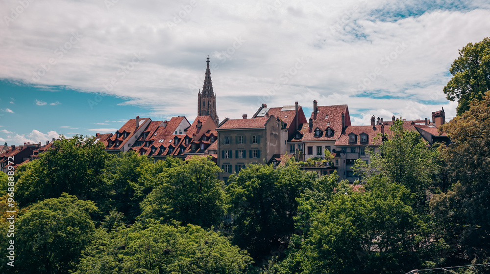 Picturesque rooftops of Bern, Switzerland, surrounded by lush greenery under a bright blue sky in early summer