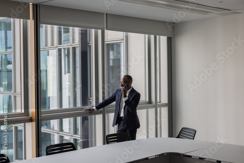 Businessman on a phone call in an empty office conference room looking out of the window