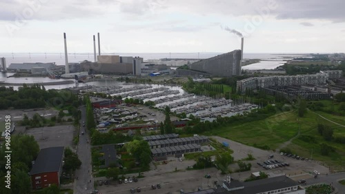 Aerial views capture Copenhagen's harbor, highlighting boats and the Amager Bakke or Copenhill waste to energy plant, which releases a plume of smoke into a cloudy summer sky photo