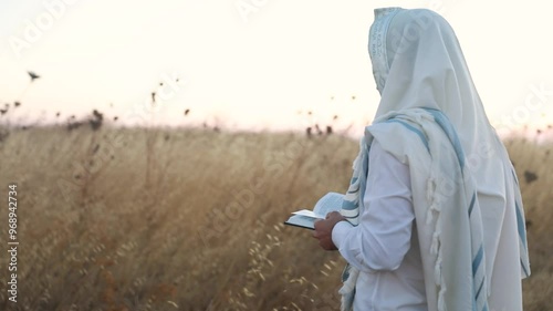 A jew prays in a field at sunrise, with tallit and Sidur. Tfilat Shacharit.
