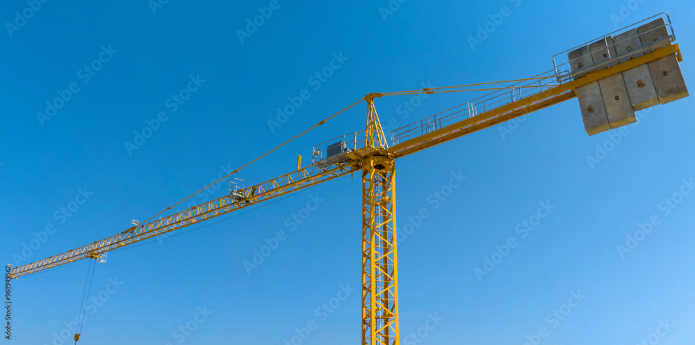 Aerial view of a yellow industrial tower crane operating in high building construction site. These large machines allow the concrete plates weight balance. City development concept. Aerial view of a yellow industrial tower crane operating in high building construction site. These large machines allow the concrete plates weight balance. City development concept.