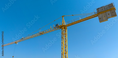 Aerial view of a yellow industrial tower crane operating in high building construction site. These large machines allow the concrete plates weight balance. City development concept. 