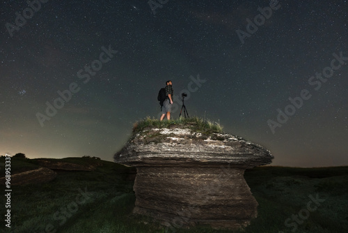 A guy landscape astrophotographer with a mirrorless camera on a tripod takes pictures in nature in the summer at night in Kostivere karstiala. Starry sky.