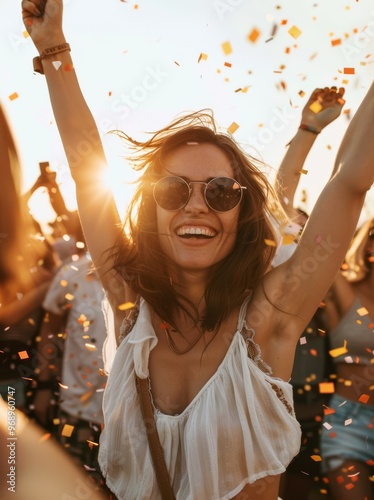 A joyful young woman wearing sunglasses with her arms raised in celebration at a summer festival, radiating happiness and carefree festival vibes