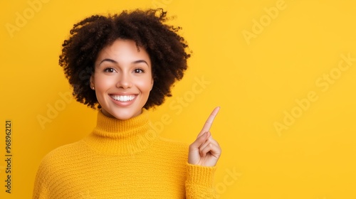 A cheerful woman wearing a yellow sweater, smiling and pointing at something on a colorful background