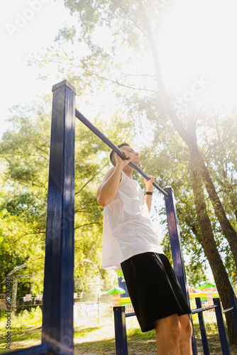 Handsome pumped up young male bodybuilder doing exercises on horizontal bar and parallel bars outdoors on the street. Beautiful male body shapes, beauty and health, training and motivation