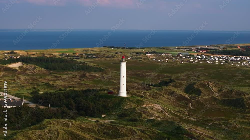 Lyngbjerg Fyr lighthouse stands tall on a sunny day, overlooking the picturesque Ringkobing Fjord. The North Sea creates a stunning backdrop against the clear blue sky Lyngbjerg Fyr lighthouse stands tall on a sunny day, overlooking the picturesque Ringkobing Fjord. The North Sea creates a stunning backdrop against the clear blue sky
