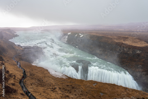 The majestic Gullfoss waterfall in Iceland, formed by the Hvita river cascading down two tiers into a narrow canyon. The powerful water flow and misty spray create a breathtaking sight. photo