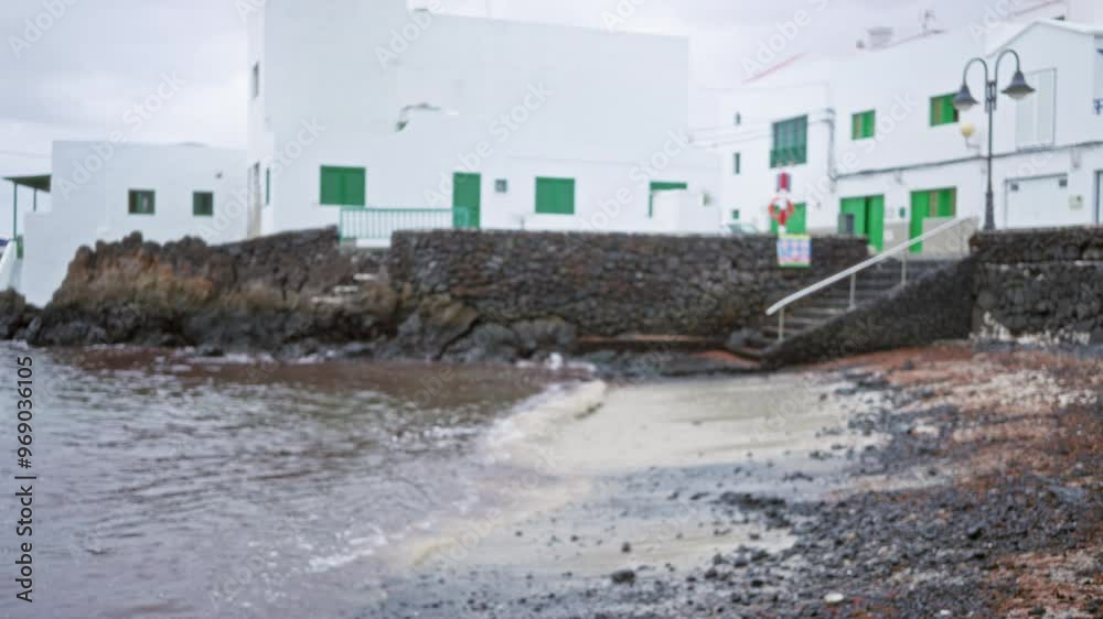 Blurred image of outdoor area in lanzarote, spain showcasing white buildings with green shutters near rocky beach in canary islands Blurred image of outdoor area in lanzarote, spain showcasing white buildings with green shutters near rocky beach in canary islands
