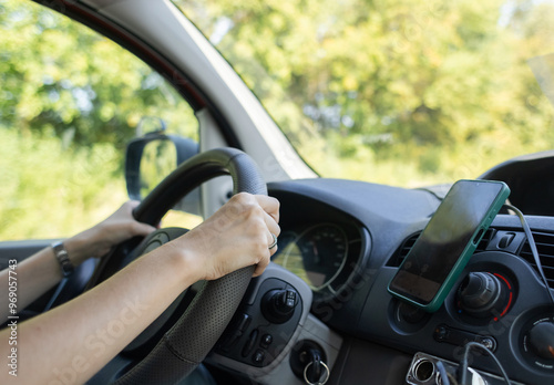 A woman drives a car and looks intently at the track. The navigator on the smartphone shows the map and the correct direction. Driving lessons on a manual transmission