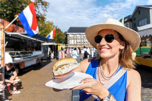 Photography Portrait young happy adult female tourist woman enjoy eating traditional Dutch sandwich with pickled matjes herring onion at local market in Groningen Netherlands