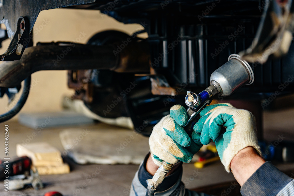 Man spraying an anti-corrosion compound on bottom of car.