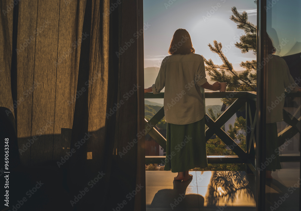 Young woman standing on balcony and admiring view of sunset or sunrise in mountains