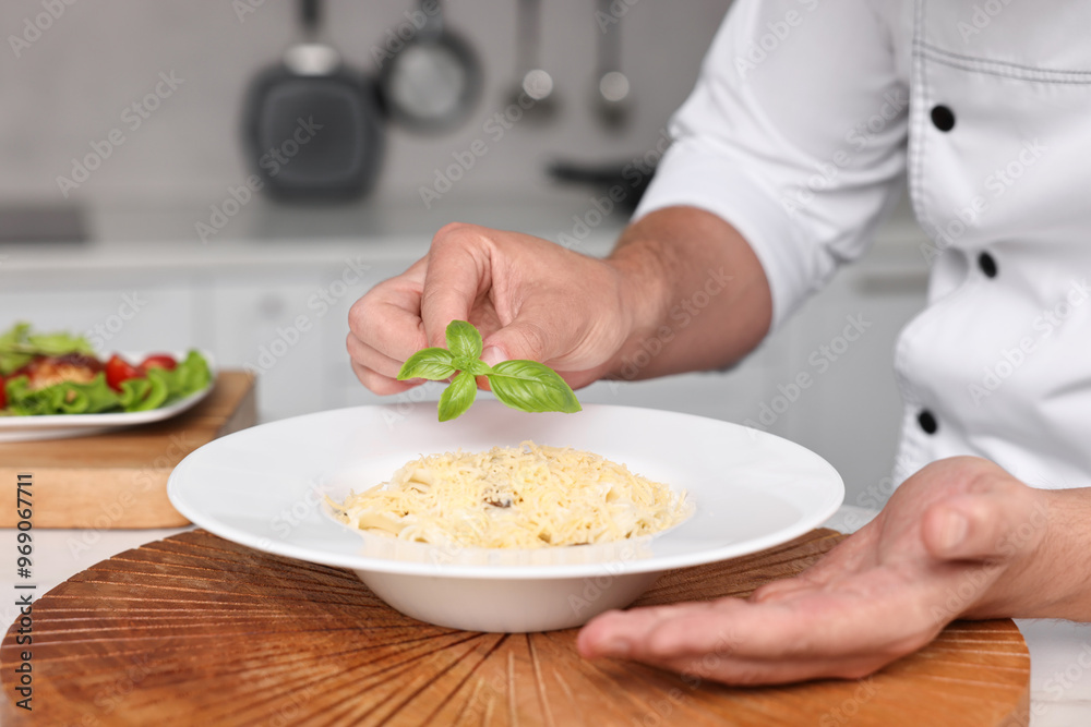 Professional chef decorating delicious pasta with basil at table in kitchen, closeup Professional chef decorating delicious pasta with basil at table in kitchen, closeup