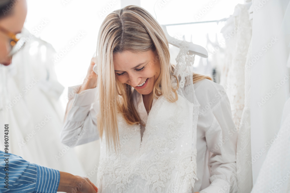 Two women browsing wedding dresses in a bridal shop, surrounded by white gowns. One woman is holding a dress while they both admire the selection. Two women browsing wedding dresses in a bridal shop, surrounded by white gowns. One woman is holding a dress while they both admire the selection.