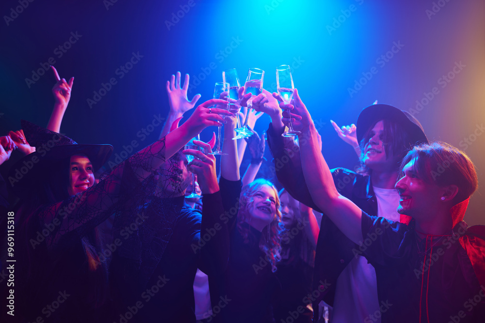 Friends, boys and girls in various Halloween costumes gathering together at nightclub for celebration raising glasses and clinking, cheerfully celebrating and having fun. Concept of Halloween, holiday Friends, boys and girls in various Halloween costumes gathering together at nightclub for celebration raising glasses and clinking, cheerfully celebrating and having fun. Concept of Halloween, holiday