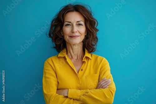 Beautiful, attractive, middle aged woman wearing casual yellow shirt with arms crossed standing isolated on blue background. with generative ai